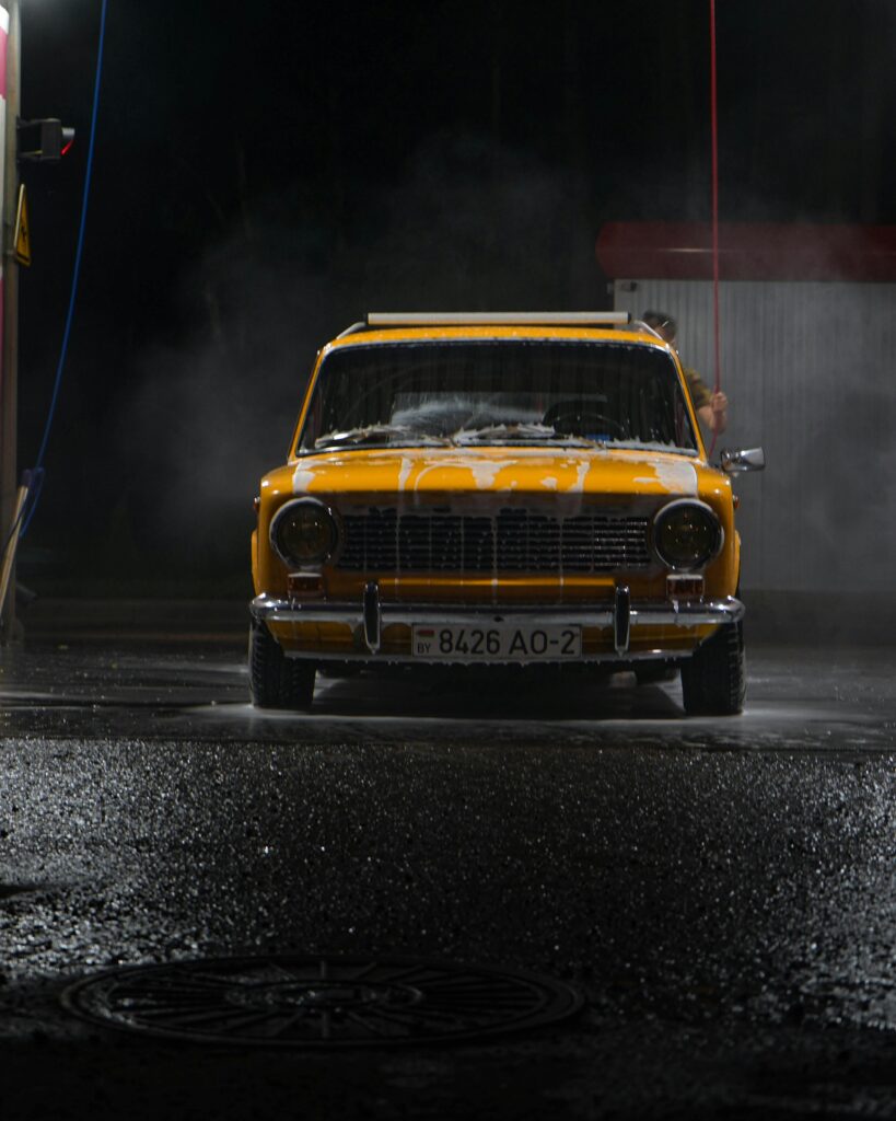 A vintage yellow car getting washed at night, emitting a moody and dramatic atmosphere.